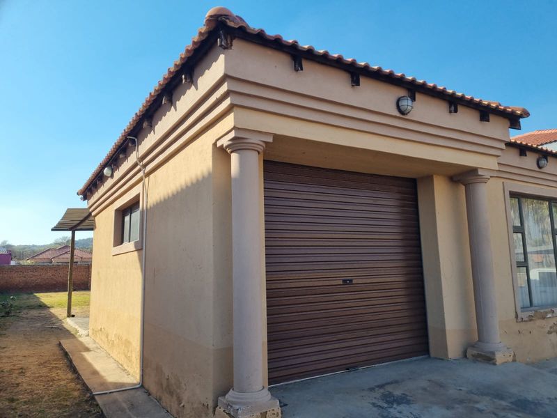 A detached garage featuring a brown roller door, decorative columns, and a tiled roof, showing signs of exterior wear and weathering.