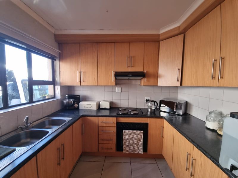 Functional kitchen featuring wood-look cabinetry, dark laminate countertops, a double stainless steel sink, and built-in cooking appliances with a tiled splashback.