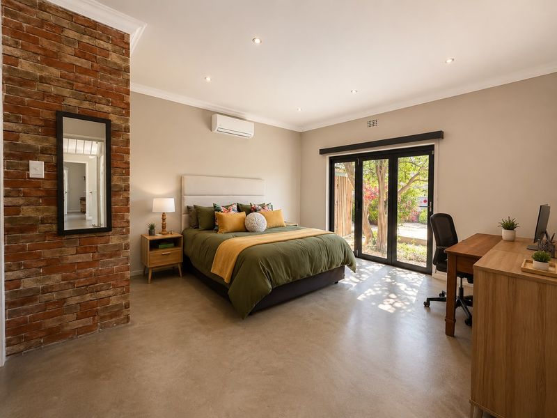 Spacious bedroom featuring a striking exposed brick wall, polished concrete floors, and large sliding doors providing direct access to the garden.