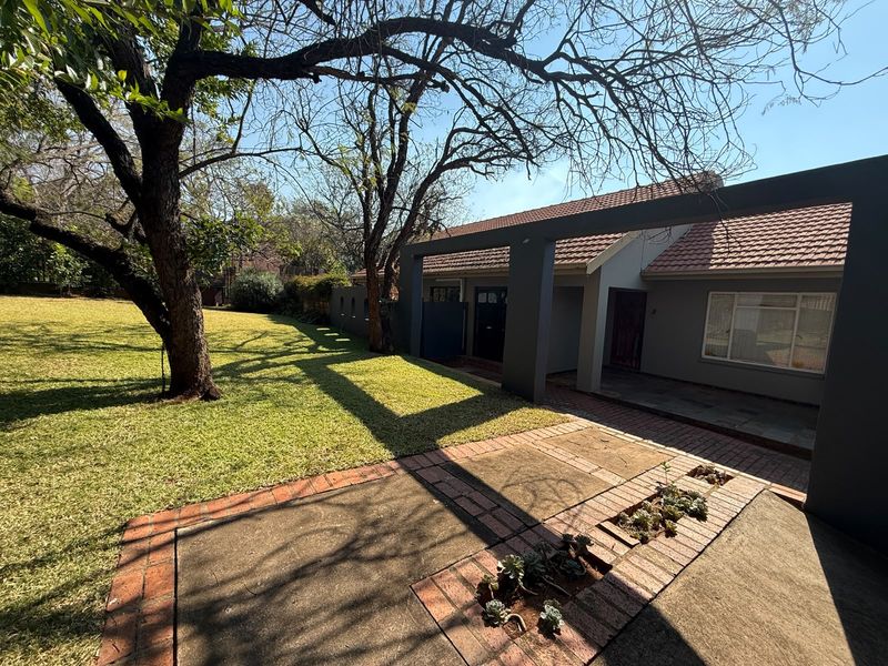 Rear view of the property featuring a covered patio area, brick paving, and a spacious established garden with mature trees.