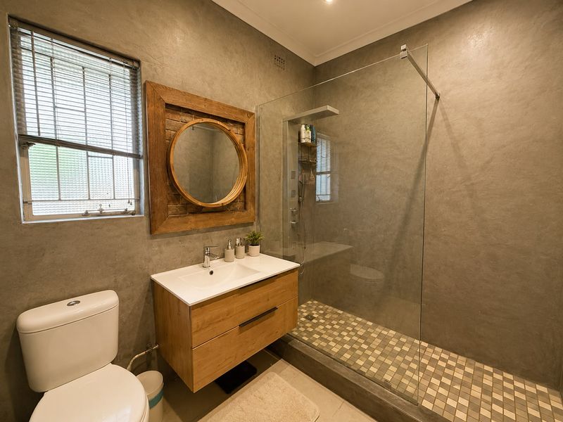 Modern bathroom featuring a walk-in shower with glass screen, floating wood-finish vanity, and contemporary cement-look wall finishes.