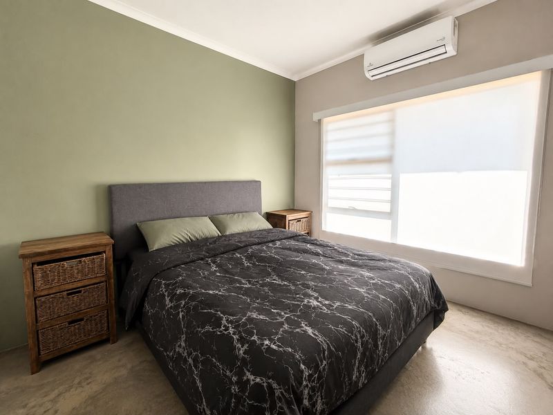 A well-maintained bedroom featuring polished concrete floors, a split-system air conditioner, and modern roller blinds for privacy.
