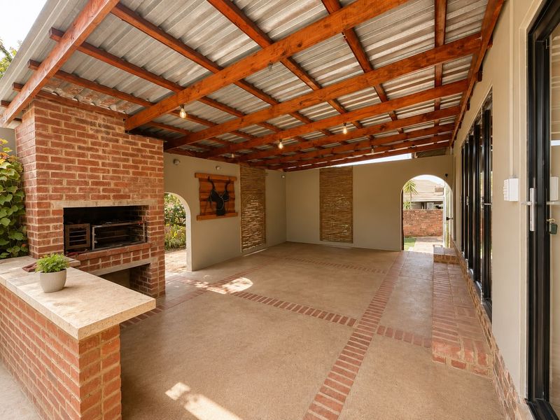 Spacious covered patio featuring a built-in brick braai, stone prep counter, exposed timber beams, and direct access to the home through sliding glass doors.