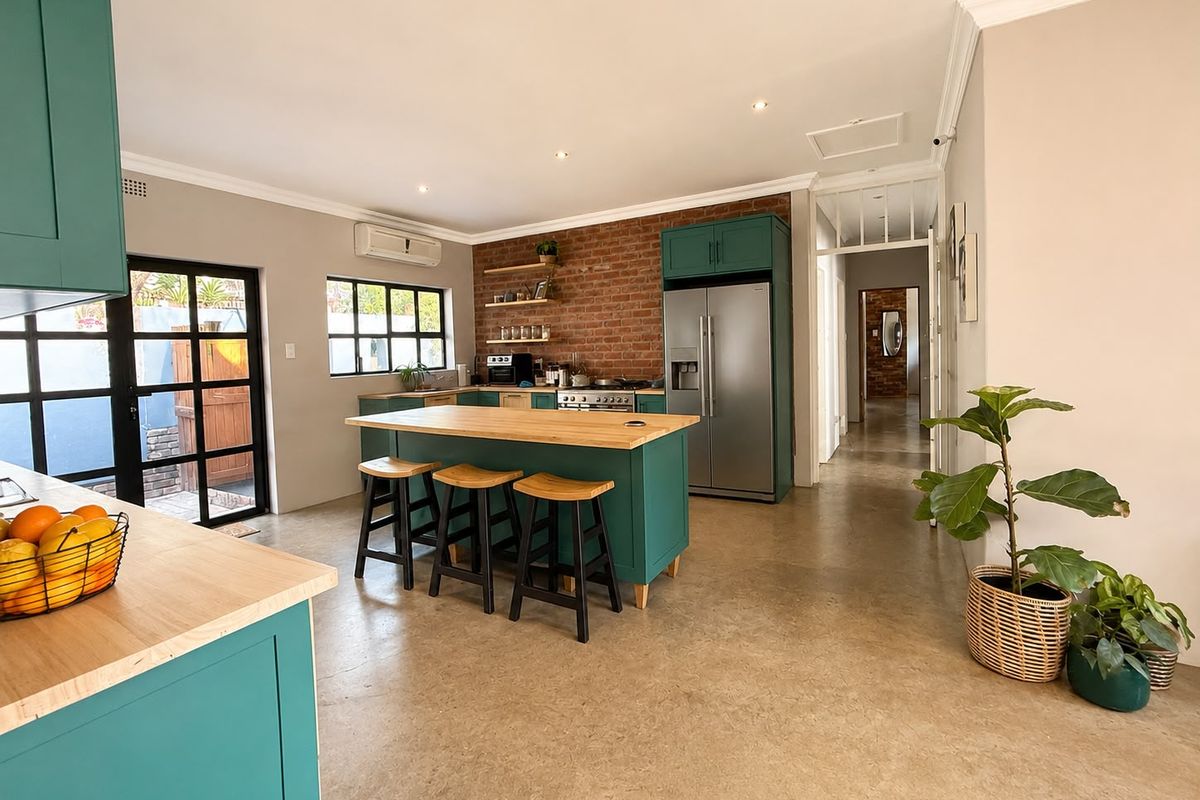 Modern kitchen featuring teal cabinetry, wooden countertops, a central island, and an exposed brick feature wall, complemented by polished concrete floors and natural light.