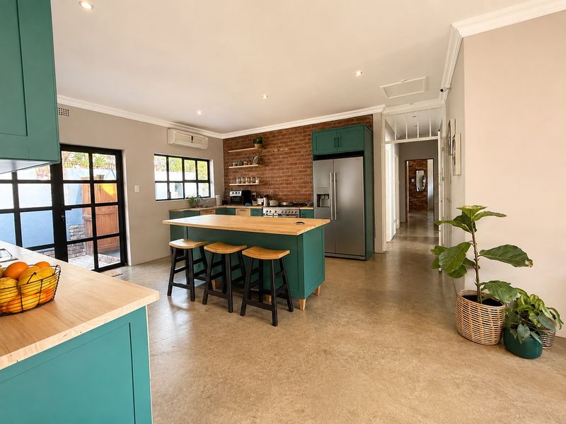 Modern kitchen featuring teal cabinetry, wooden countertops, a central island, and an exposed brick feature wall, complemented by polished concrete floors and natural light.