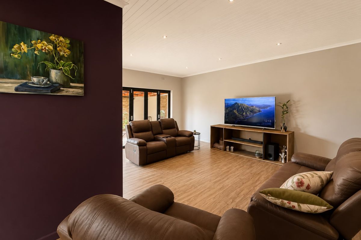 Spacious living room featuring timber laminate flooring, recessed downlighting, and bi-fold doors leading to an outdoor area.