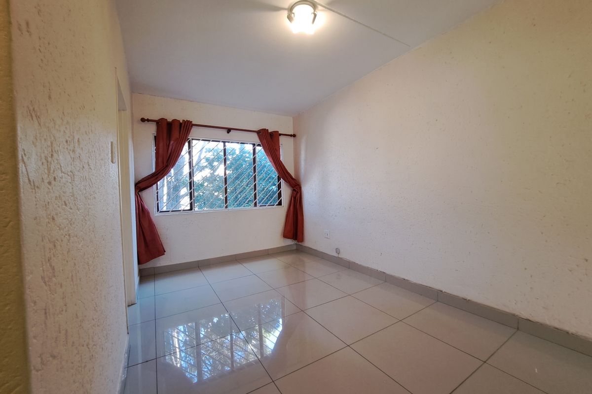 An empty bedroom featuring tiled flooring, security bars on the window, and a neutral wall finish, ready for personalization.