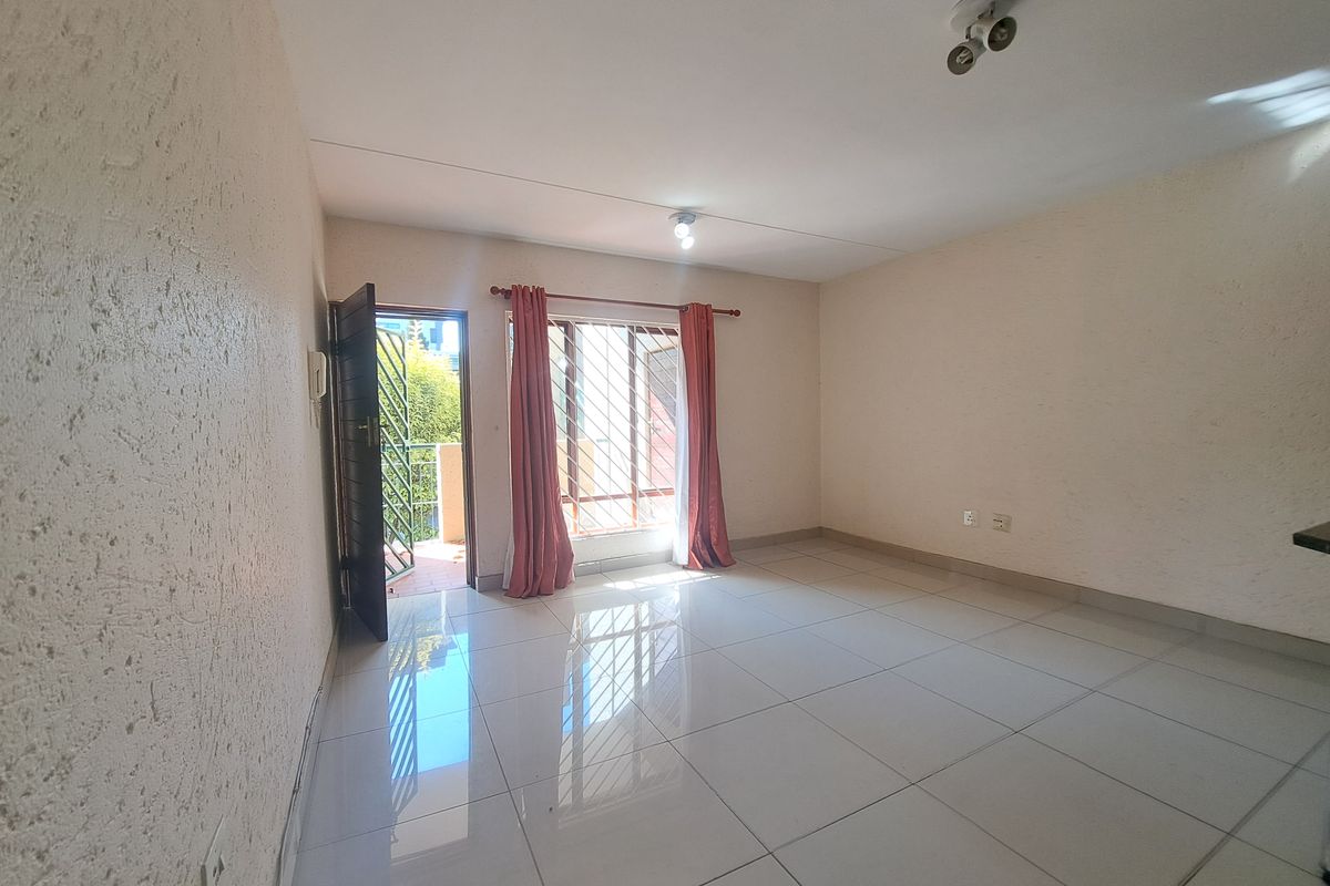 A bright, empty living room featuring tiled flooring, a security gate leading to a balcony, and security bars on the windows.