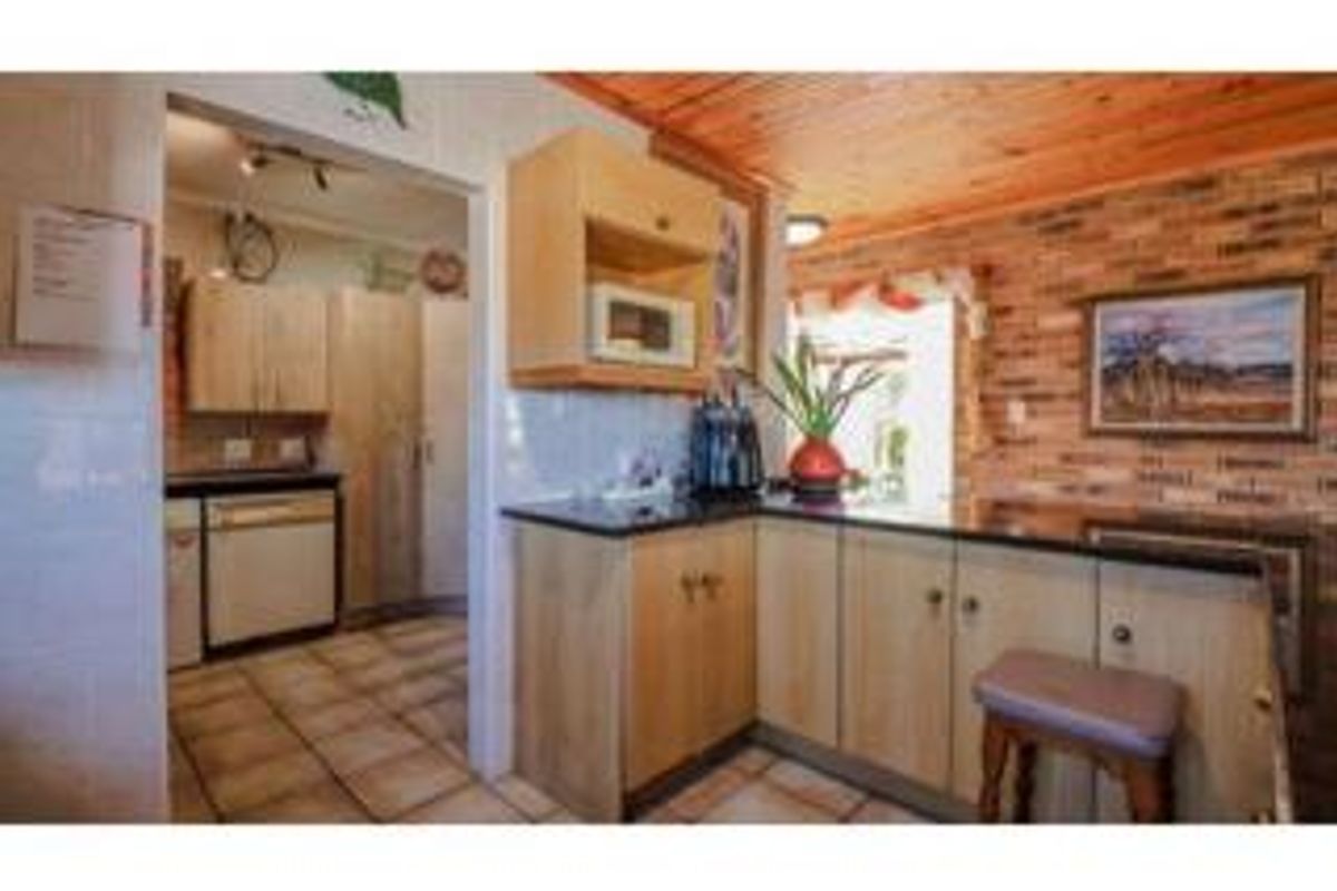 A functional kitchen featuring light wood cabinetry, granite countertops, and a distinctive exposed brick wall with a timber ceiling.