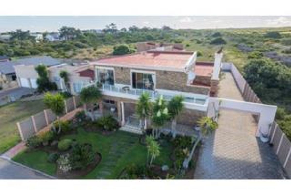 Aerial view of a multi-level residential property featuring stone cladding, a tiled roof, a paved driveway, and a landscaped front garden.