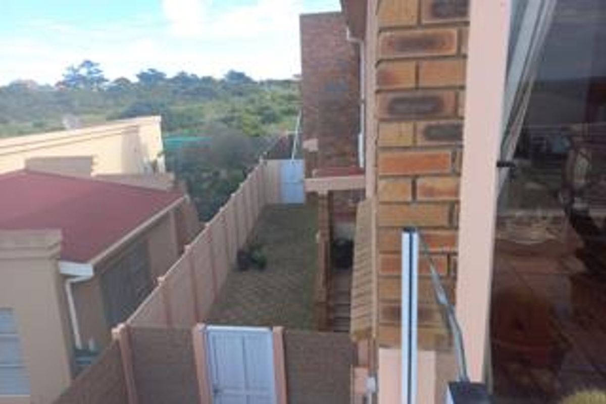 An elevated view of the rear exterior area, featuring a brick facade, boundary wall, and a pedestrian gate leading to a side pathway.