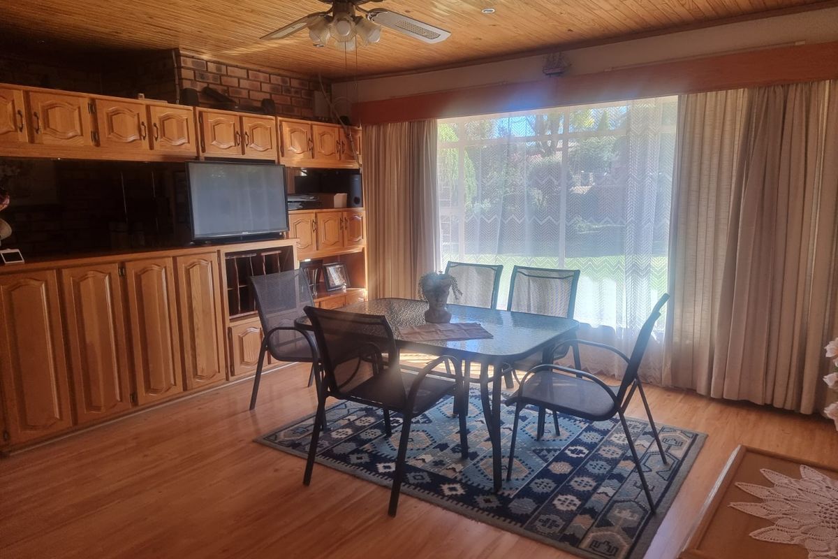 A living area featuring extensive built-in wooden cabinetry, a timber-clad ceiling with a ceiling fan, and large windows overlooking the garden.