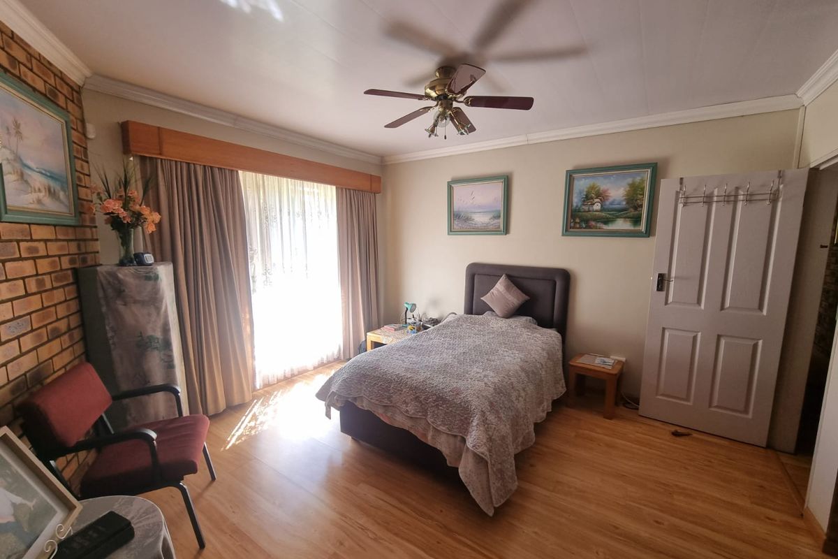 A bedroom featuring wood-look laminate flooring, a ceiling fan, and a brick feature wall, with natural light entering through large window curtains.
