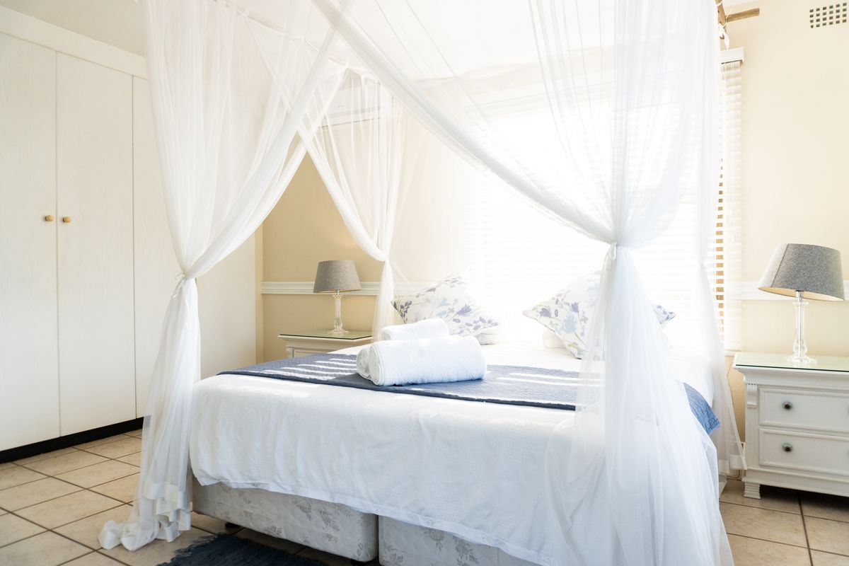 A bright bedroom featuring built-in wardrobes, tiled flooring, and a window with fitted blinds.