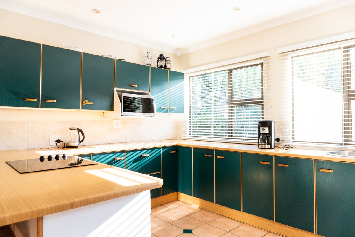 A functional kitchen featuring dark green cabinetry, light wood-look countertops, tiled backsplash, and a built-in electric hob.