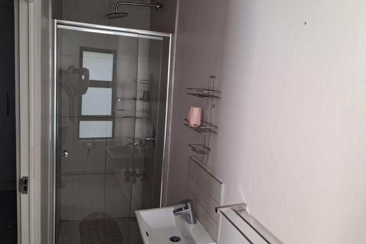 A compact, modern bathroom featuring a glass-enclosed shower with a rain shower head and a wall-mounted basin with chrome fixtures.