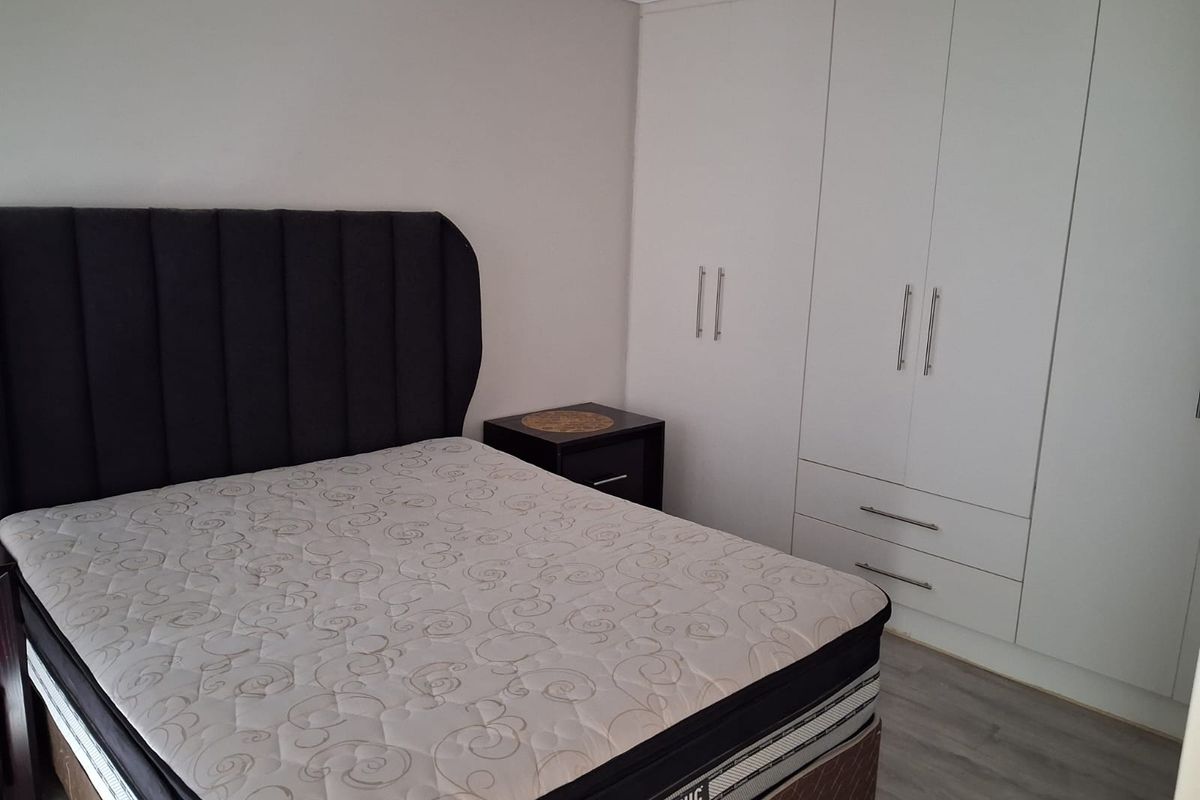 A well-maintained bedroom featuring modern white built-in cupboards, neutral wall finishes, and durable laminate flooring.
