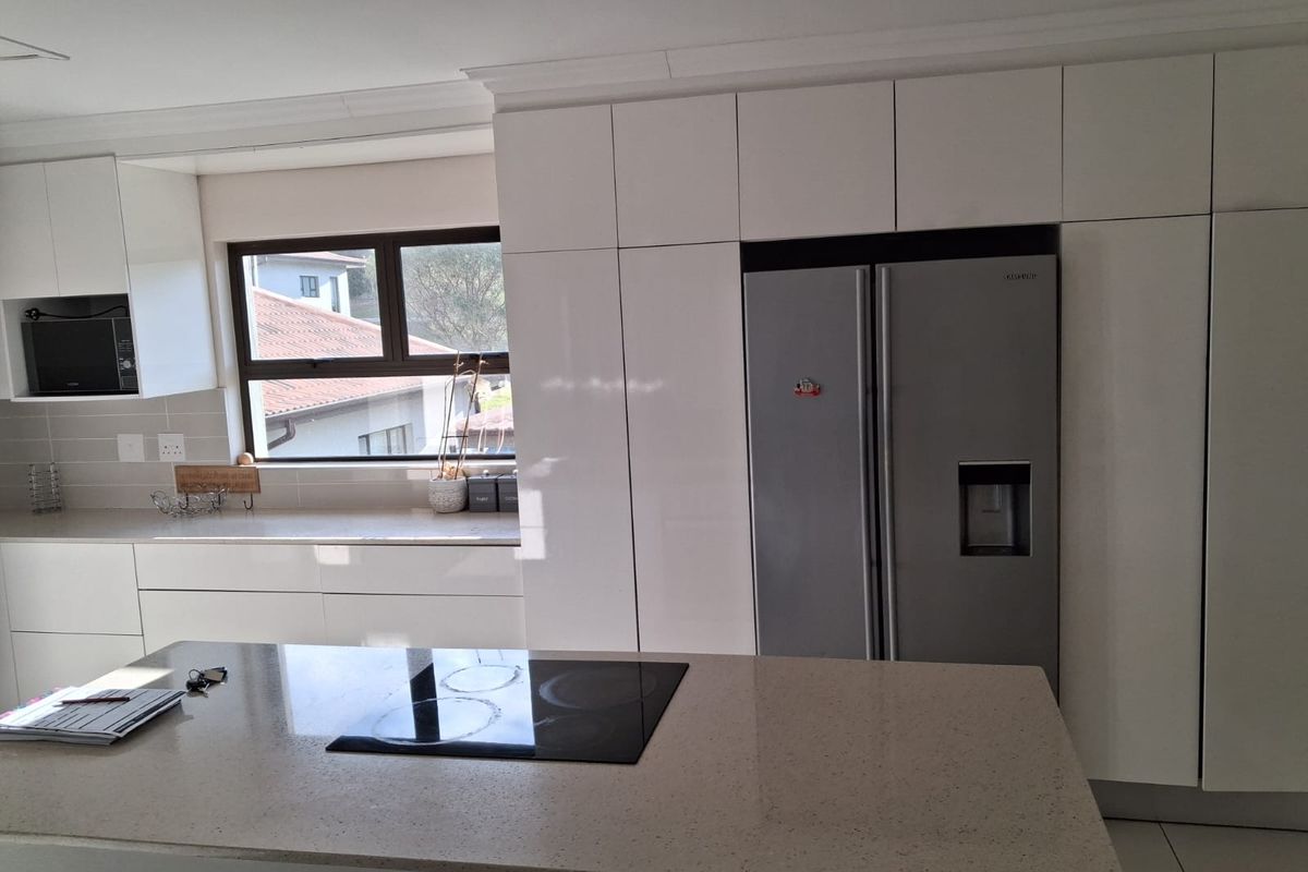 Modern kitchen featuring sleek white cabinetry, stone countertops, a central island with an integrated electric hob, and high-quality built-in appliances.