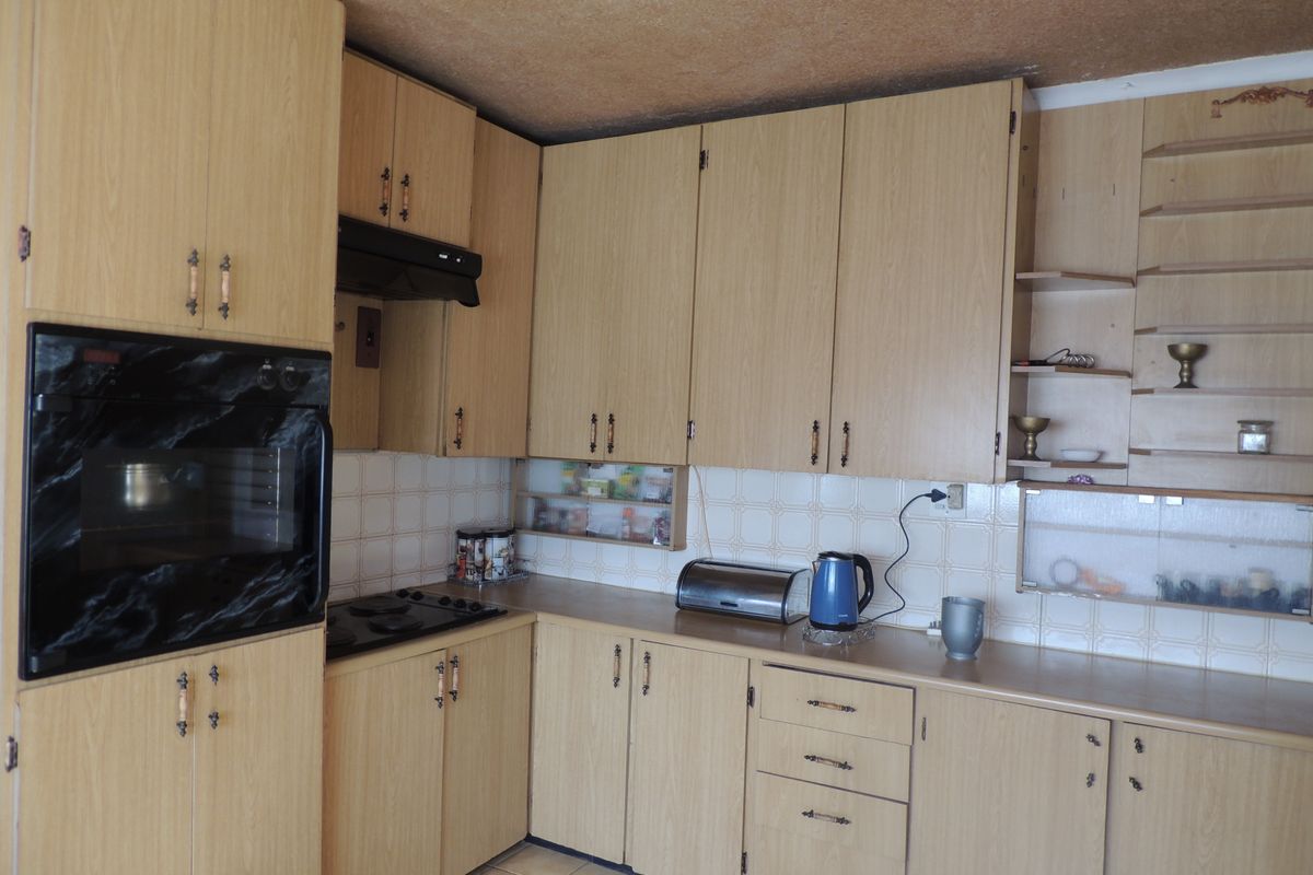 A dated kitchen featuring laminate cabinetry, built-in oven, hob, and extractor fan, with a tiled backsplash and visible ceiling staining.