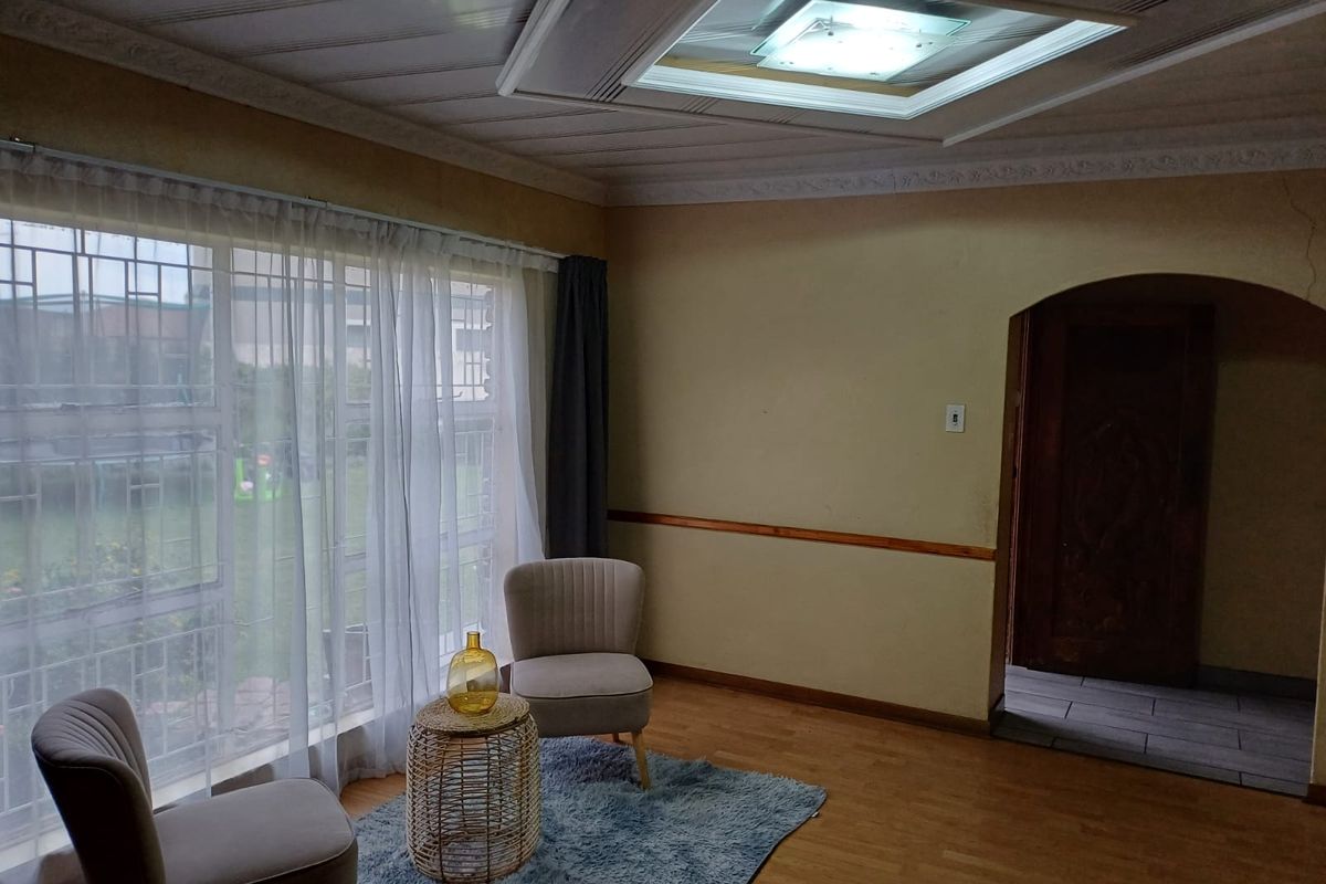 A living room featuring laminate flooring, large windows with security bars, and an arched doorway leading to an adjacent space.