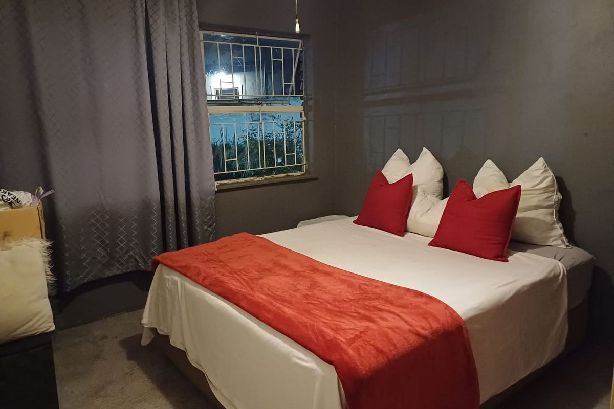 A bedroom featuring dark painted walls, a window with security bars, and basic flooring.