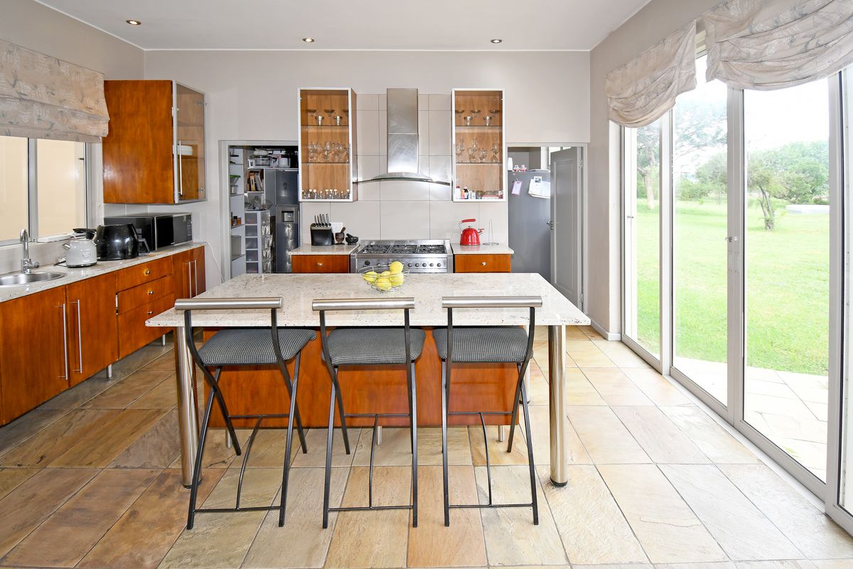 Spacious kitchen featuring wooden cabinetry, granite countertops, a central island with breakfast bar, stainless steel extractor fan, and direct access to the garden.