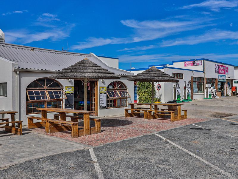 Front exterior view of a commercial property featuring a paved patio area with built-in timber seating and thatched umbrellas.