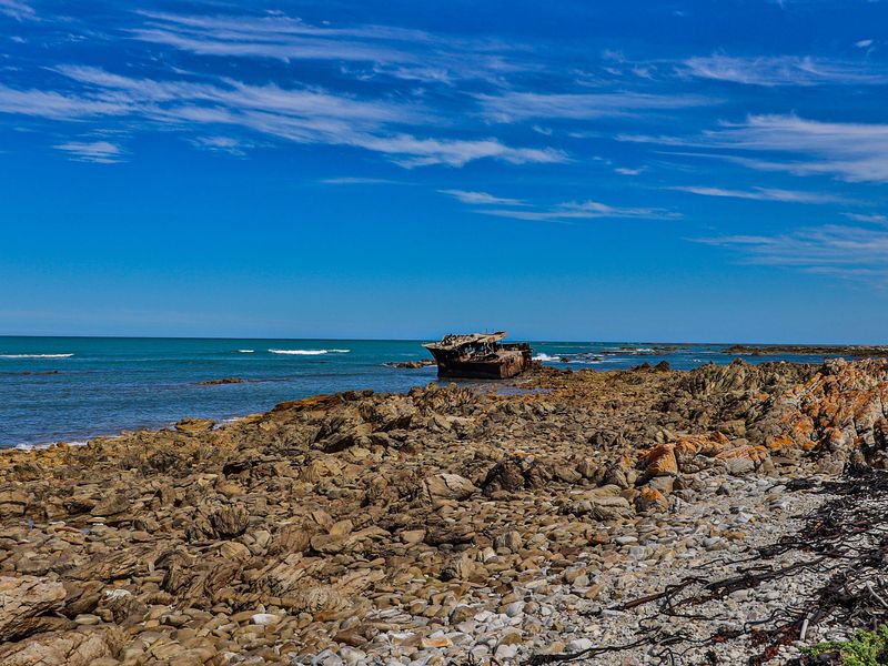 A scenic view of a rocky coastline featuring a shipwreck visible in the distance against the ocean horizon.