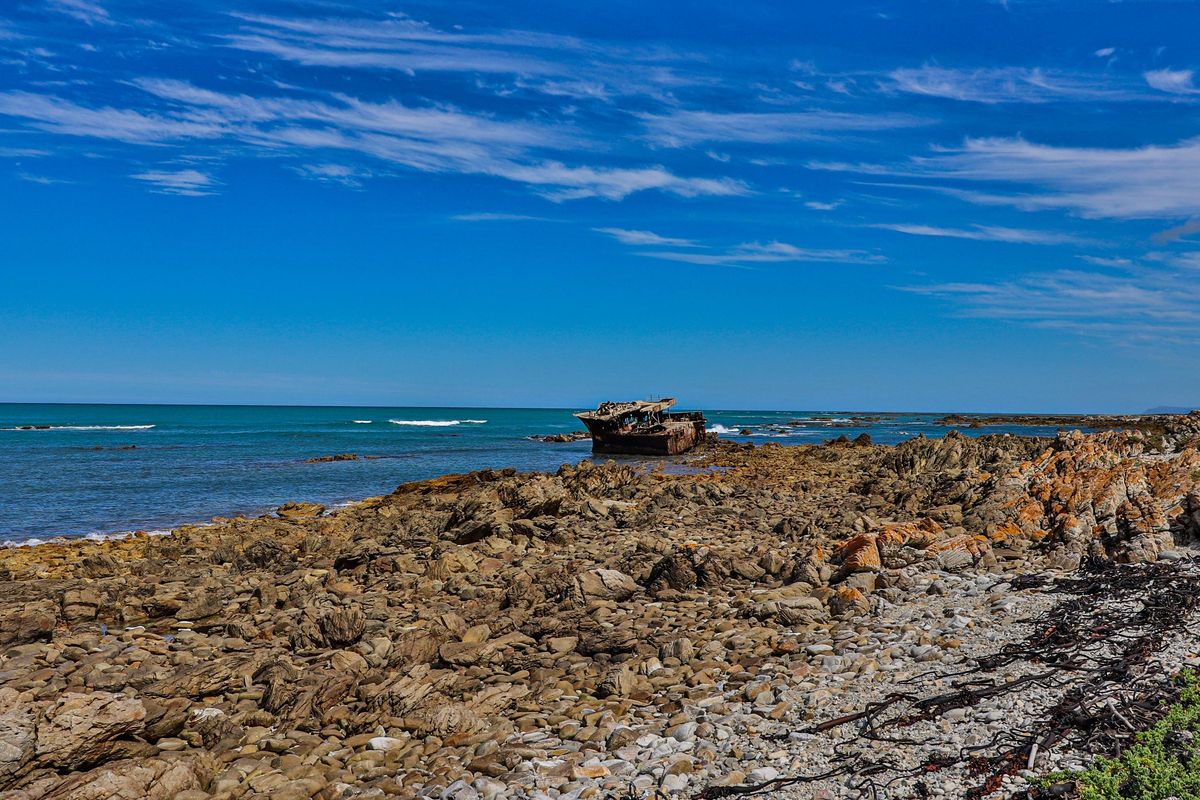 A scenic view of a rocky coastline featuring a shipwreck visible in the distance against the ocean horizon.
