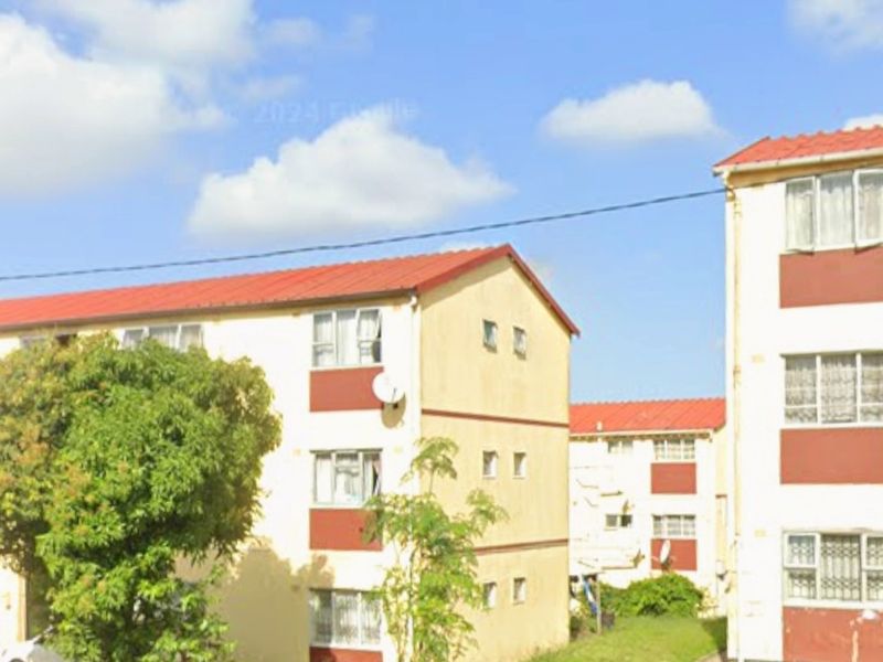 Exterior view of multi-story apartment blocks featuring pitched roofs, metal window frames with security bars, and weathered exterior finishes.