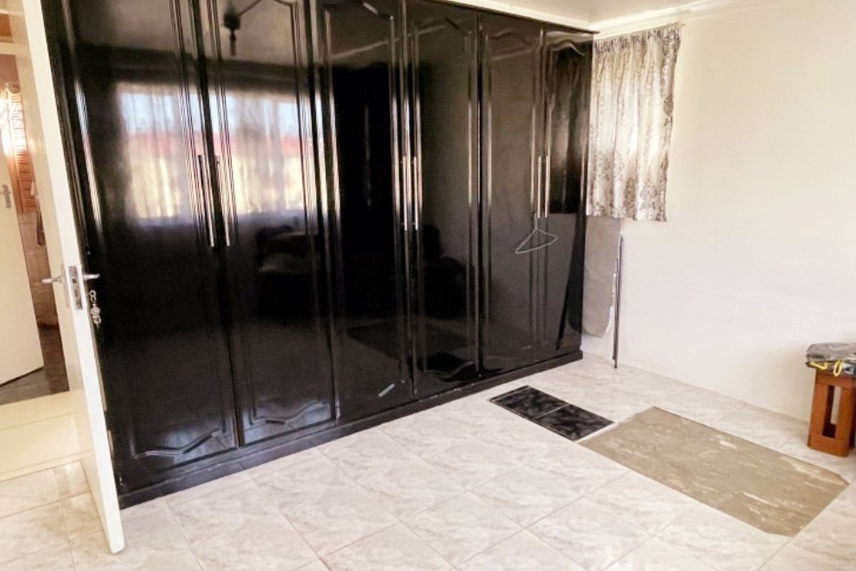 A bedroom featuring large, dark built-in cupboards and neutral tiled flooring, offering a clean and functional space ready for personalization.