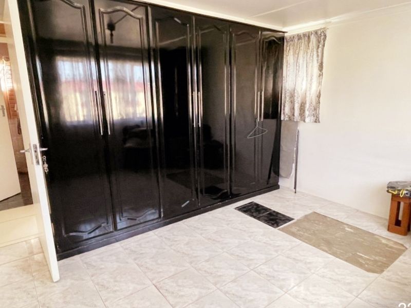 A bedroom featuring large, dark built-in cupboards and neutral tiled flooring, offering a clean and functional space ready for personalization.