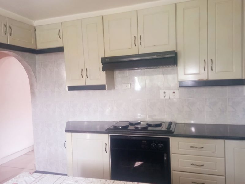 A functional kitchen featuring built-in cabinetry, a dark countertop, integrated oven, electric hob, and an extractor fan with a tiled backsplash.