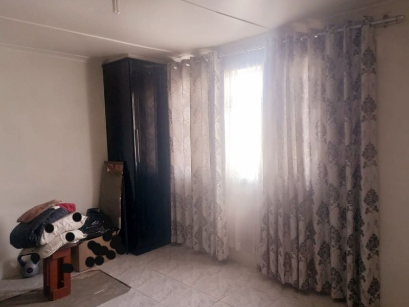 A bedroom featuring tiled flooring and a built-in cupboard, with natural light entering through a window dressed with curtains.