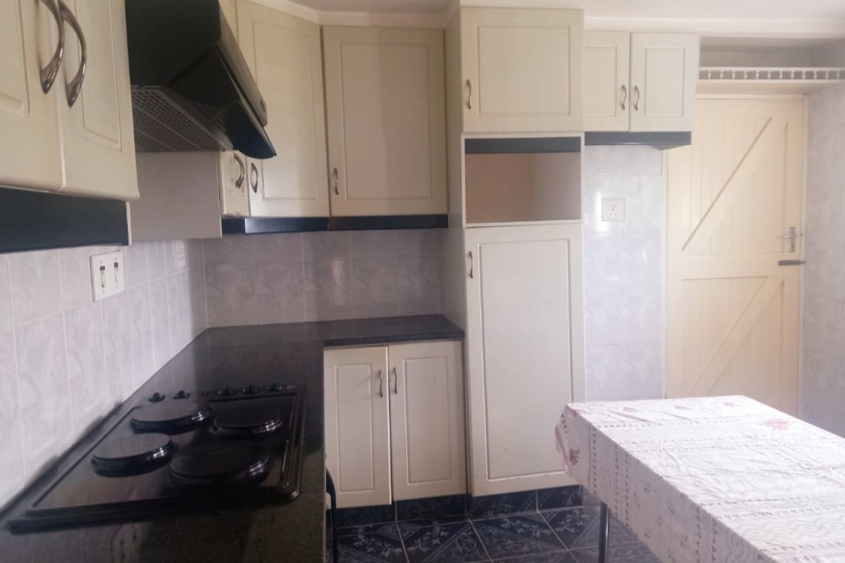 A functional kitchen featuring built-in cabinetry, granite countertops, an electric hob with extractor fan, and tiled finishes throughout.