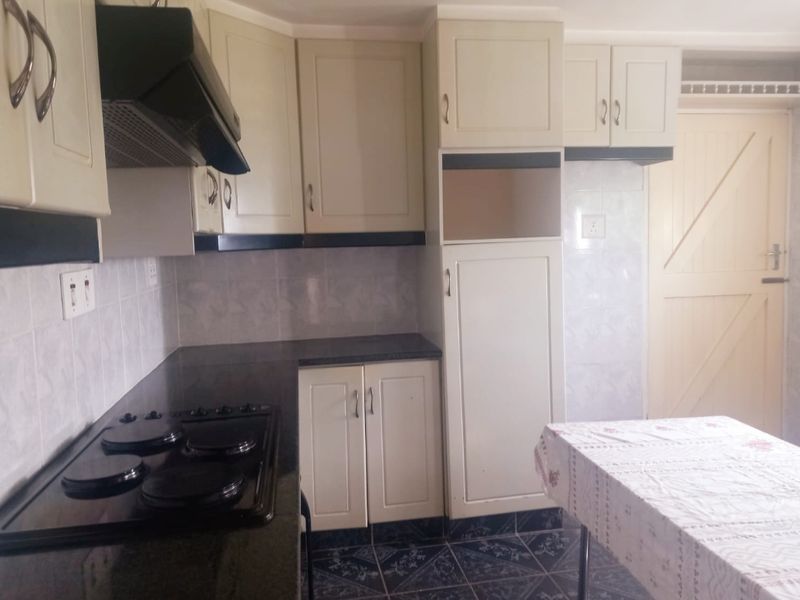 A functional kitchen featuring built-in cabinetry, granite countertops, an electric hob with extractor fan, and tiled finishes throughout.