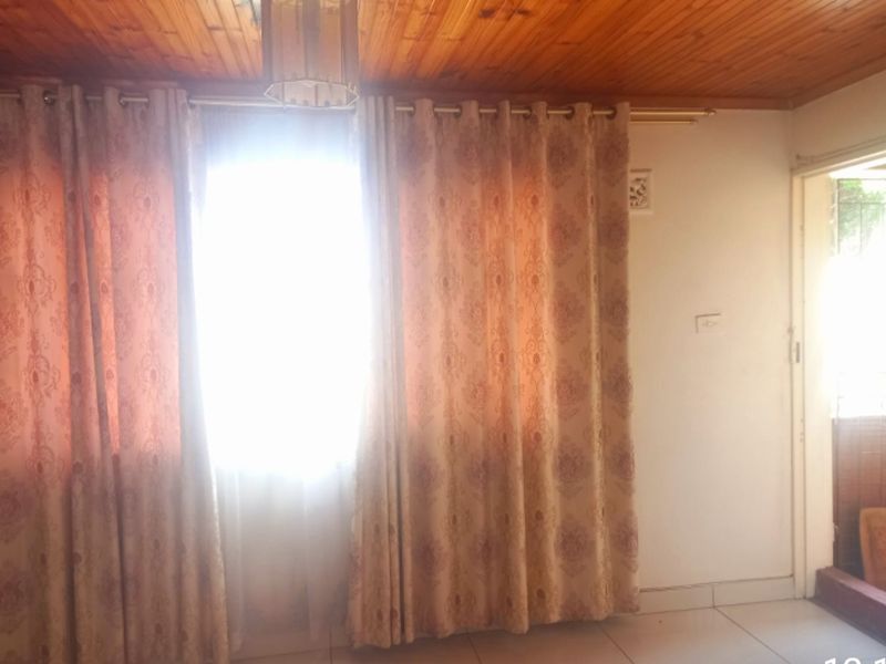 A living area featuring a timber ceiling and tiled flooring, with natural light entering through a window and an adjacent doorway.
