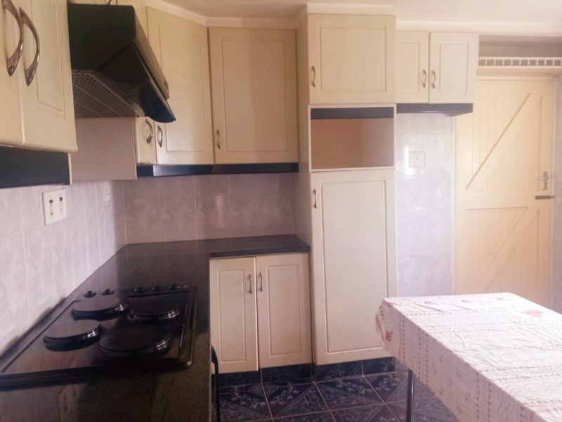 A functional kitchen featuring built-in cabinetry, granite countertops, an electric hob with extractor fan, and tiled finishes throughout.