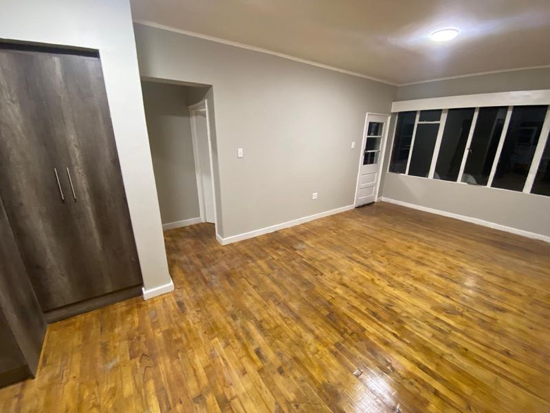 An empty living room featuring original wooden parquet flooring, a built-in cupboard, and large windows providing natural light.