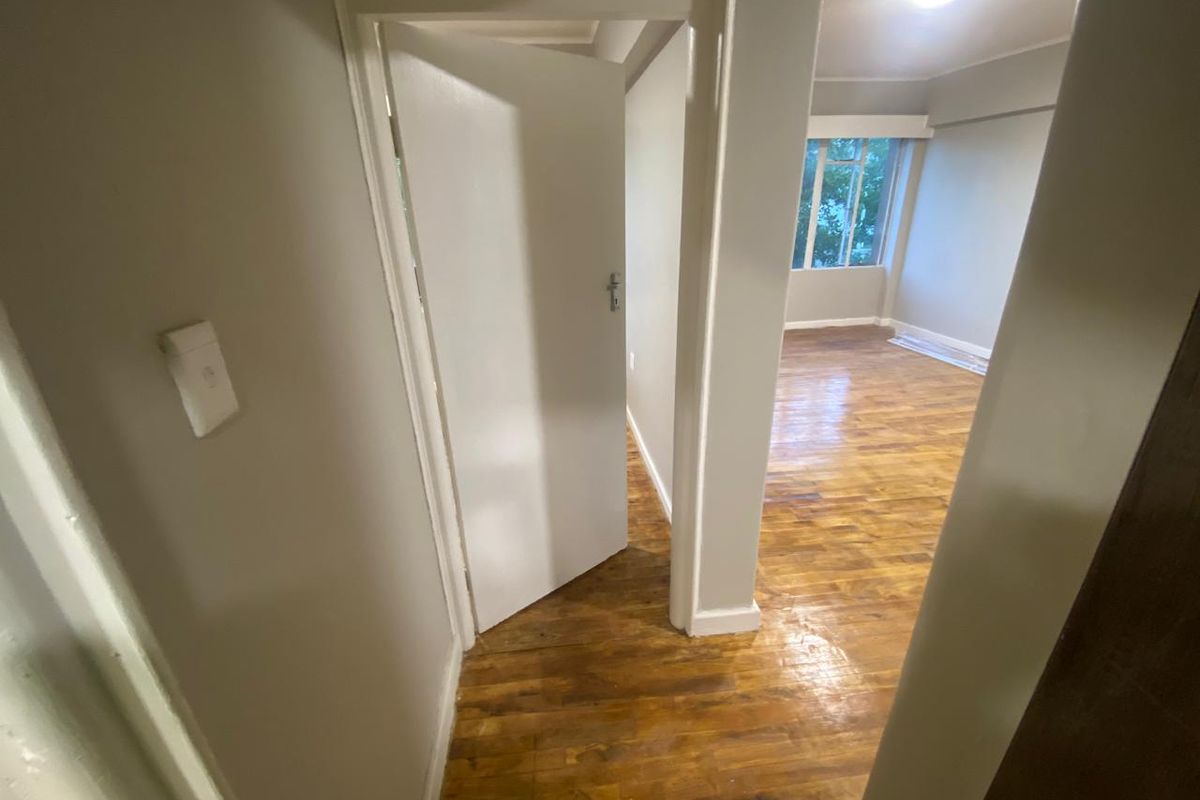 A view from a hallway looking into an empty room featuring polished hardwood flooring and neutral wall finishes.