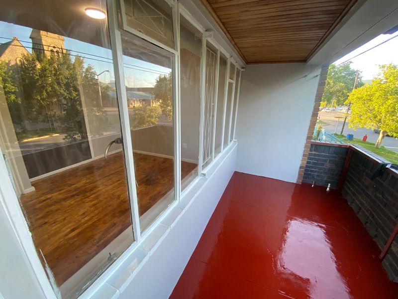 A covered balcony featuring a timber ceiling, painted concrete flooring, and large windows overlooking the street.