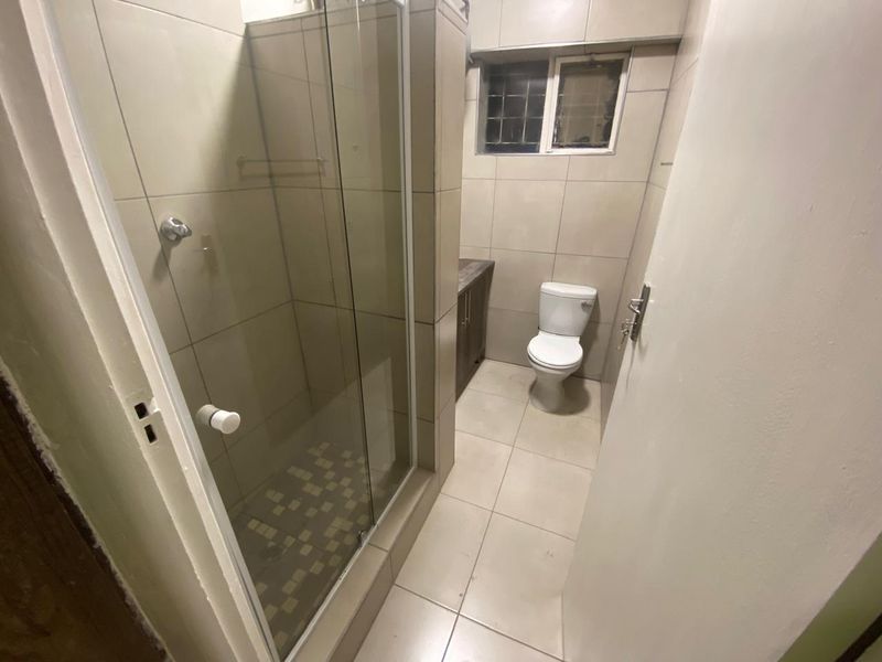 A functional bathroom featuring a glass-enclosed shower, toilet, and built-in vanity with neutral wall and floor tiling.