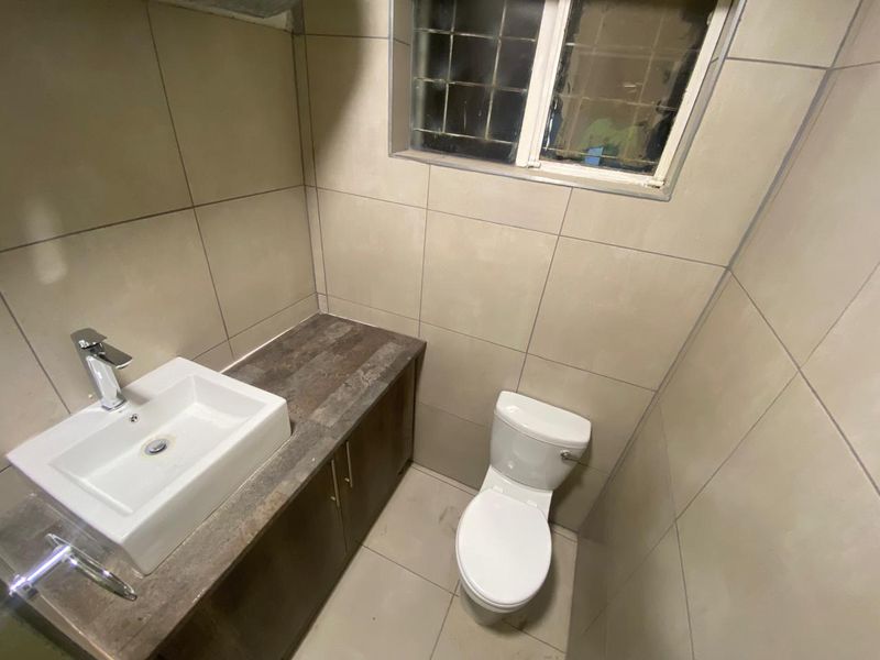 A compact bathroom featuring a modern vessel sink on a vanity cabinet, a standard toilet, and neutral wall and floor tiling.