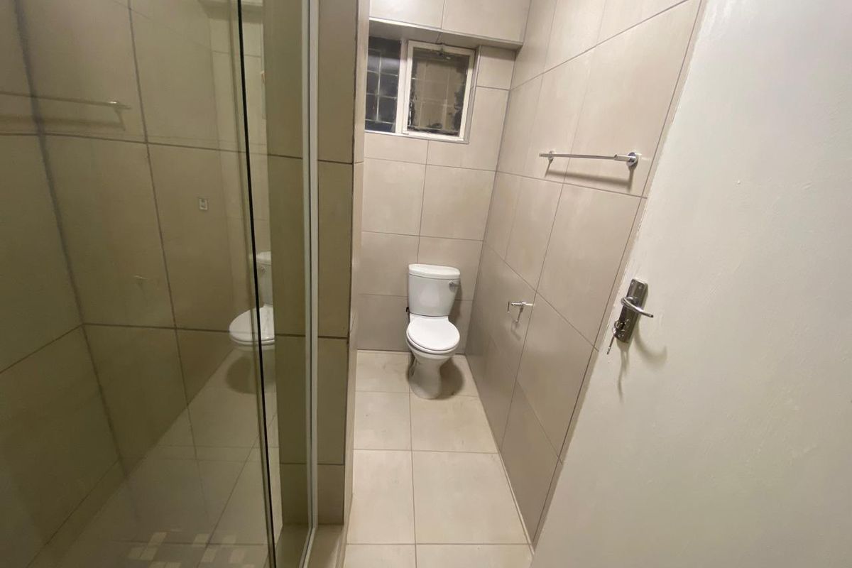 A functional bathroom featuring a glass-enclosed shower, a standard toilet, and neutral floor-to-ceiling wall tiling.