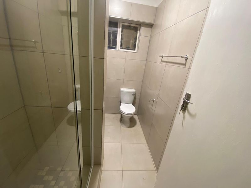 A functional bathroom featuring a glass-enclosed shower, a standard toilet, and neutral floor-to-ceiling wall tiling.
