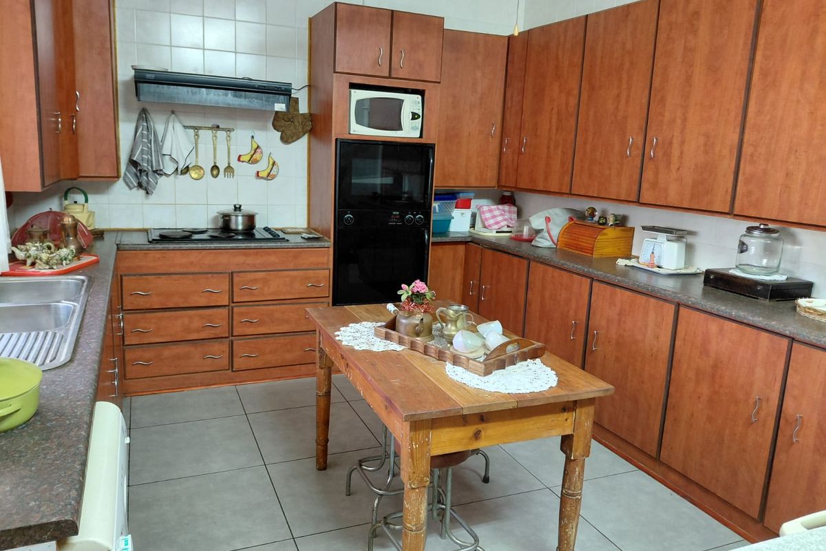 A functional kitchen featuring extensive wooden cabinetry, built-in oven, microwave, and hob with an extractor fan, complemented by tiled flooring and countertops.