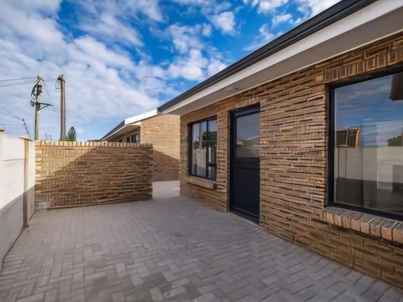 A well-maintained rear exterior view of the townhouse featuring a paved patio area, textured brick facade, and modern aluminium window and door frames.