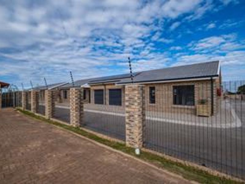 A modern townhouse exterior featuring a brick facade, tiled roof, paved driveway, and secure electric fencing with stone-clad pillars.
