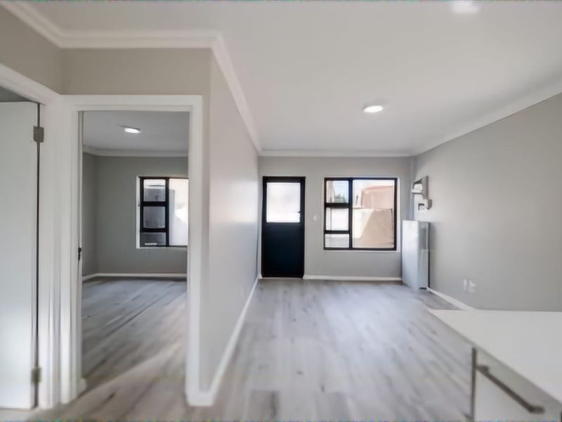 A bright, open-plan living area featuring modern laminate flooring, neutral walls, and large aluminium-framed windows, offering a clean and versatile space.