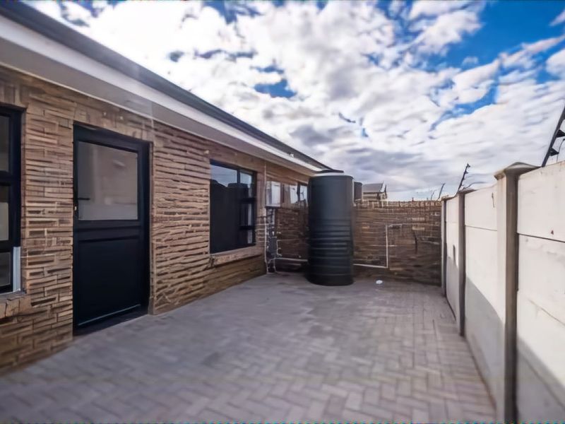 A paved rear courtyard area featuring a water storage tank, secure boundary walling with electric fencing, and direct access to the home via an aluminium door.